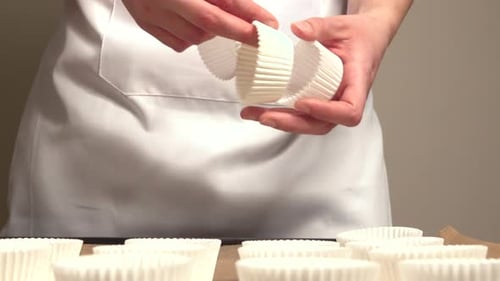 Woman placing muffin molds on tray with brown baking paper.
