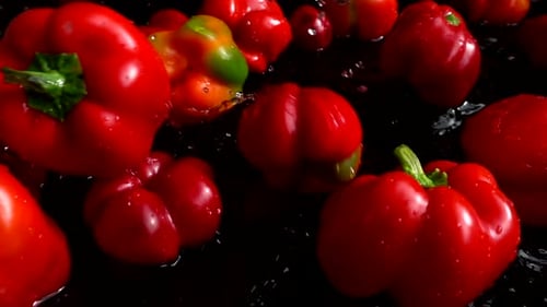 Red Bell Peppers Splashing in Water on Black Surface