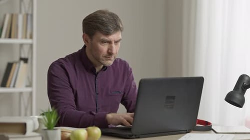 Man Typing on Laptop at Desk Indoors