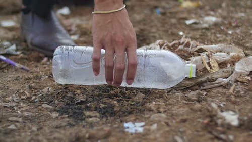 Hand Picking Up Plastic Bottle From Trashy Ground