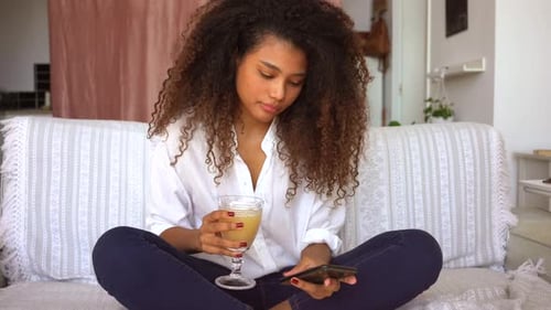 Young Woman Sitting, Drinking, and Using Cellphone