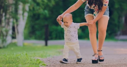 Kid Walks with His Mother By the Hands on the Path in the Summer. Happy Childhood, the First Steps