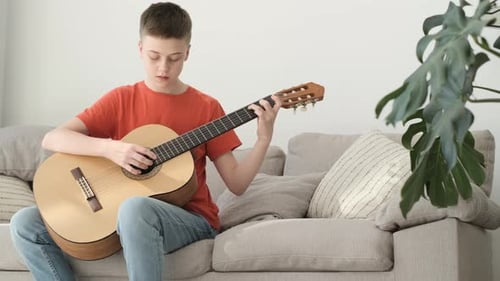 Teen Boy Plays Guitar on Couch at Home