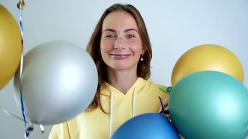 Happy Woman Holding Balloons Smiling in Front of White Wall