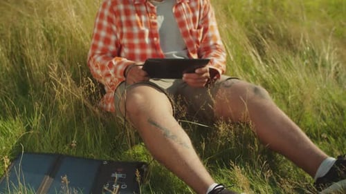 Bel homme afro-américain travaillant en réseau sur une tablette PC alimentée par un chargeur solaire dans la nature