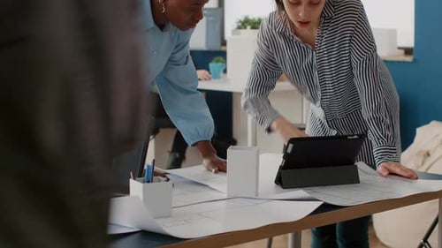 Close Up of Diverse Women Analyzing Blueprints Plan with Digital Tablet Doing Teamwork for Project