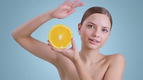 Retrato de una mujer bonita sosteniendo la mitad de una naranja y sonriendo mientras mira a la cámara