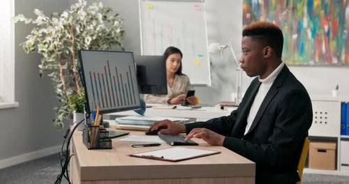 A Focused Darkskinned Man in Suit Spends Time at Work in Front of Office Computer Completing Charts