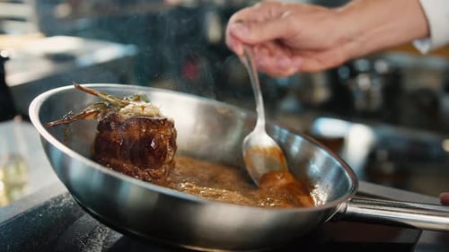 Close-up: Chef pouring sauce over filet mignon while cooking