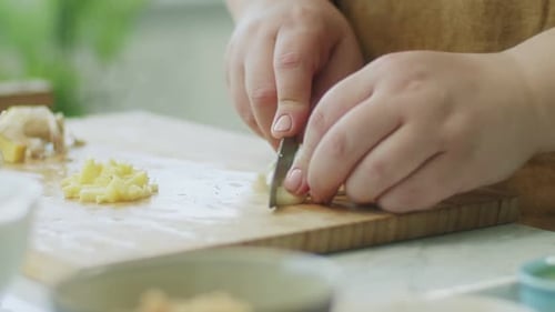 Mujer cortando ajo en tabla de madera en cocina