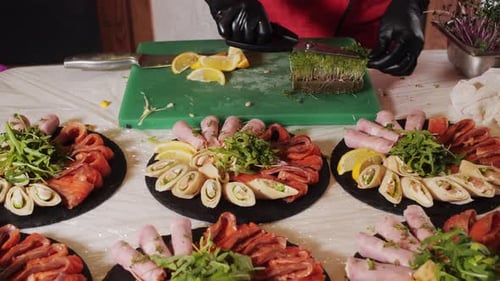 Closeup of a Plate with Snacks of Rolls Fish Cuts and Vegetables with Greens