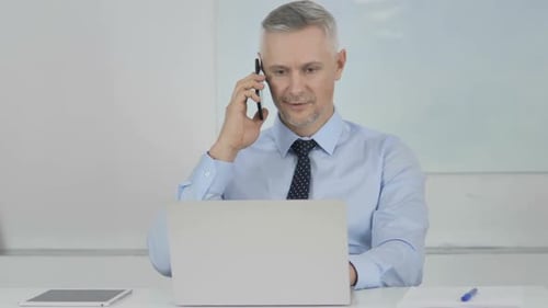Man Answers Phone While Using Laptop at Desk