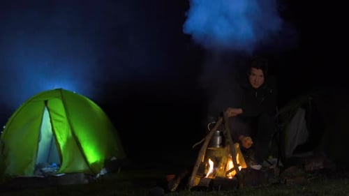 Camper Sitting by Fire with Pot at Night