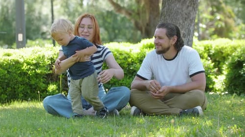 Family Spend Time in the Park Sitting on the Grass and Mother Hugging Her Son