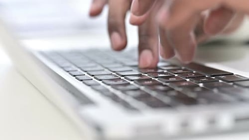 Vorderansicht der Finger eines afrikanischen Mannes, der auf der Laptoptastatur