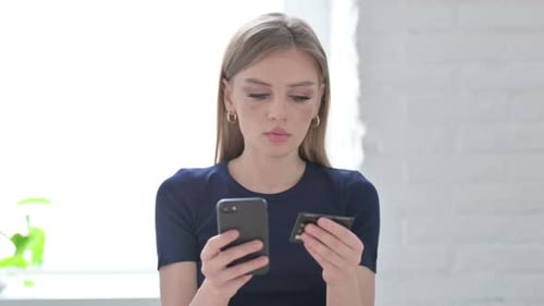 Young Woman Looks Confused Using Phone and Card