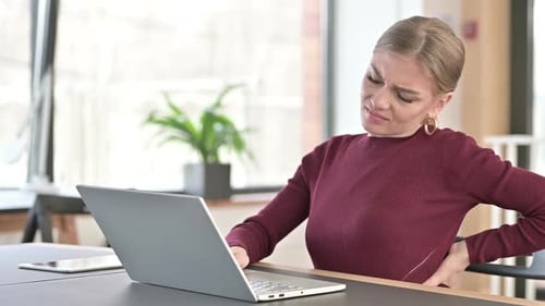 Young Woman with Back Pain Using Laptop in Office