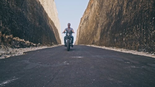 Motorcyclist Driving His Motorbike Between Two Rocks on the Ocean Beach