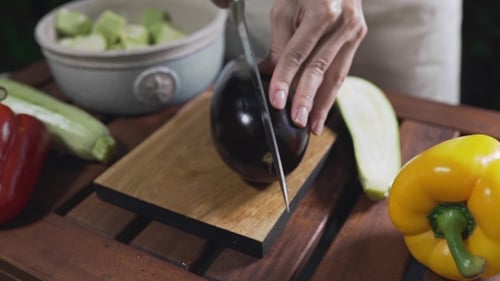 Der Koch schneidet die Aubergine draußen auf dem Holzbrett, um vegetarische Mahlzeiten und Gemüseküche zuzubereiten