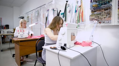 Young Seamstress and Aged Tailor at Work in Tailor Shop Working Together