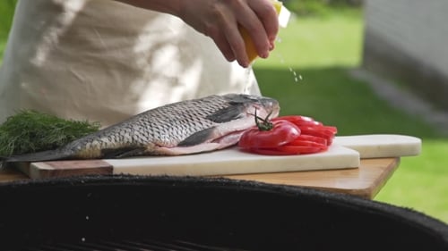 Raw Carp Is Sprinkling with Lemon Juice in Front of the Fire of Grill, Preparations for the Barbecue