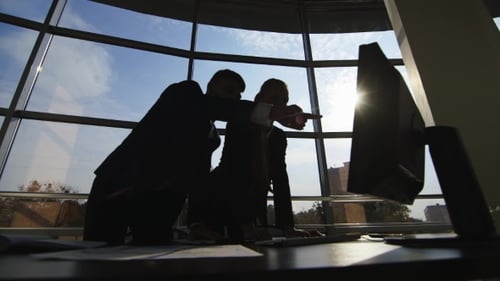 Silhouettes of Two Businessmen Working with a Computer on a Window Background in a Big Bright Office