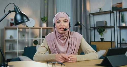 Mujer árabe en hiyab con auriculares que está sentada frente a la cámara y graba un blog