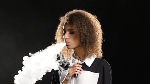 Woman Exhaling Vapor from Electronic Cigarette in Studio Woman Exhaling Vapor from Electronic Cigarette in Studio
