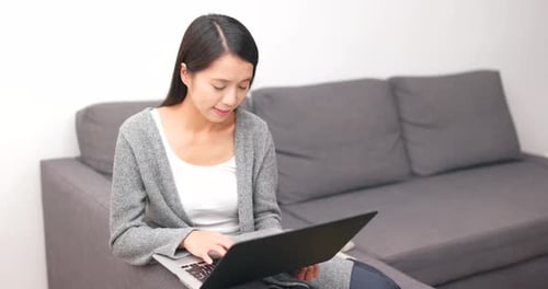 Woman Using Laptop Computer on Gray Couch at Home