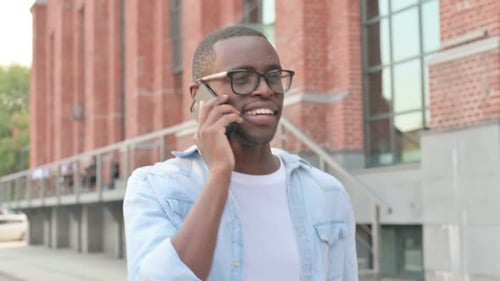 African Man Talking on Smartphone While Walking in Street Side View