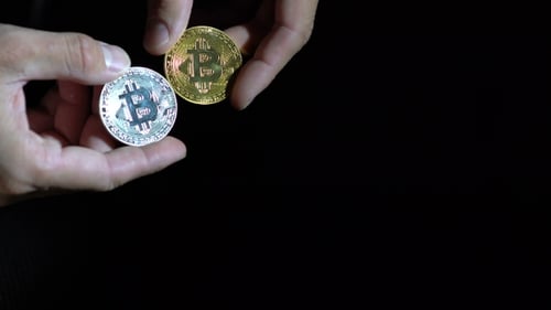 Männerhände halten goldenen und silbernen Bitcoin auf schwarzem Hintergrund