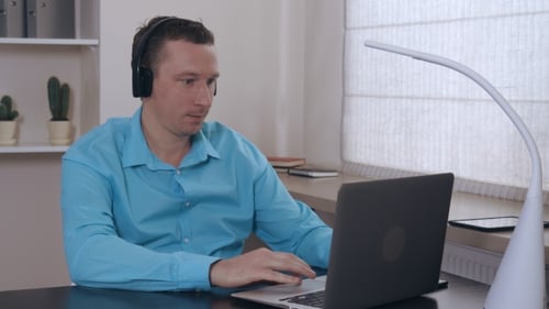 Man Wearing Headphones Typing on a Laptop