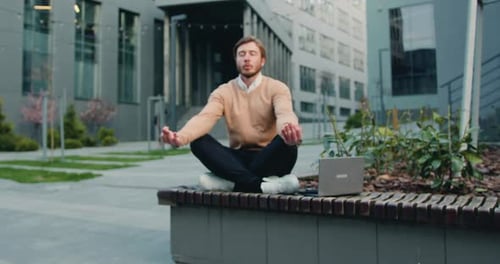 Man in Glasses Sitting in the Lotus Position on the Bench of the Courtyard of Office Building