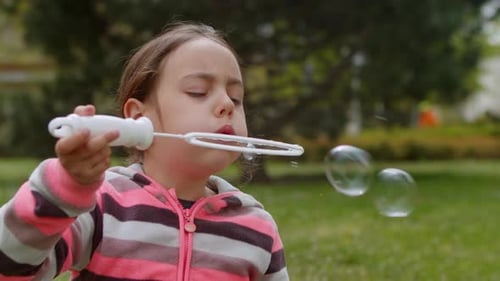 Girl Blowing Bubbles in a Green Park