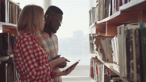 Students Reading Book Together in Library Stacks