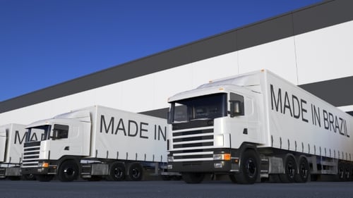 Freight Semi Trucks with MADE IN BRAZIL Caption on the Trailer Loading or Unloading