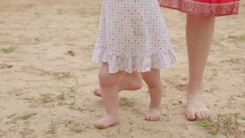Child Taking First Steps on the Beach with Parent