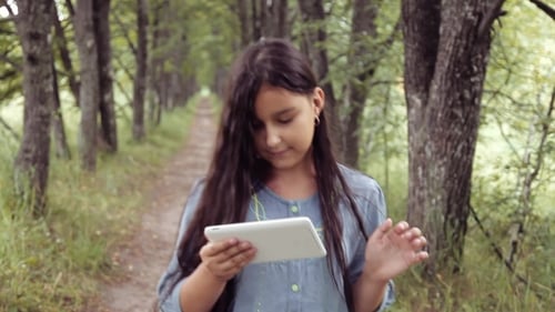 Portrait. A Beautiful Girl Is Walking in Nature Using a Tablet