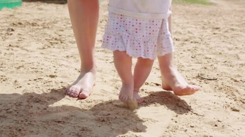 Child Learning to Walk on Sandy Beach with Adult