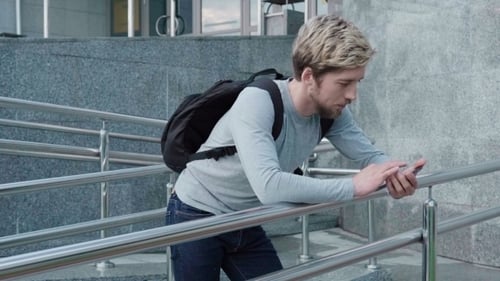 Man Leans on Railing Using Mobile Phone in City