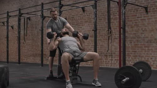 Man Doing Dumbbell Bench Press Assisted by Trainer