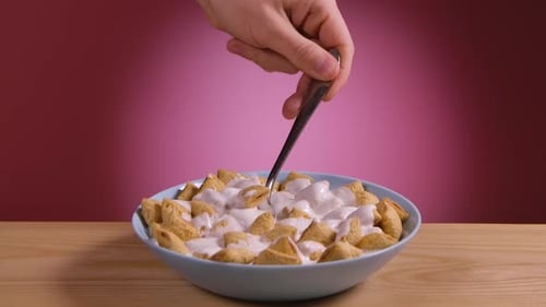 With the Help of a Spoon a Man's Hand Picks Up Crunchy Corn Pads Filled with Yogurt