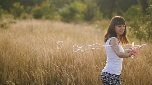 Woman Blowing Bubbles in a Grassy Field on Sunny Day