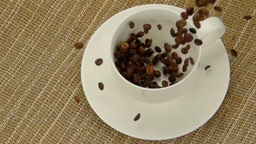 Coffee Beans Falling Into White Cup and Saucer