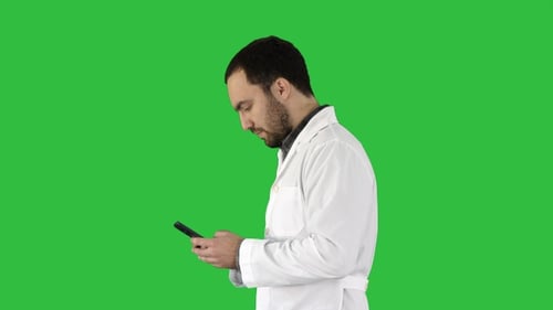 Walking doctor or nurse texting on a cell phone on a Green