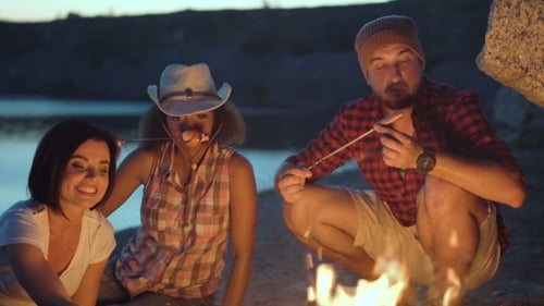 Friends Cooking Sausages Over Campfire at Night