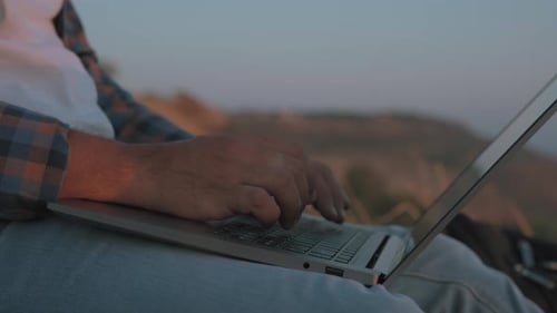 Person Typing on Laptop Outdoors at Sunrise