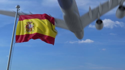 Spanish Flag Waving with Passenger Airplane Flying in Clear Blue Sky