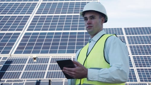 Solar Panel Technician Using Tablet Near Array