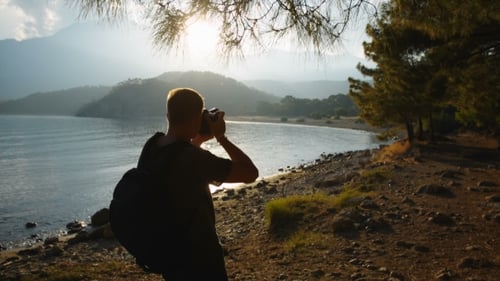 Traveler Photographer Shoots Beautiful Sunset on the Shore of a Mountain Lake